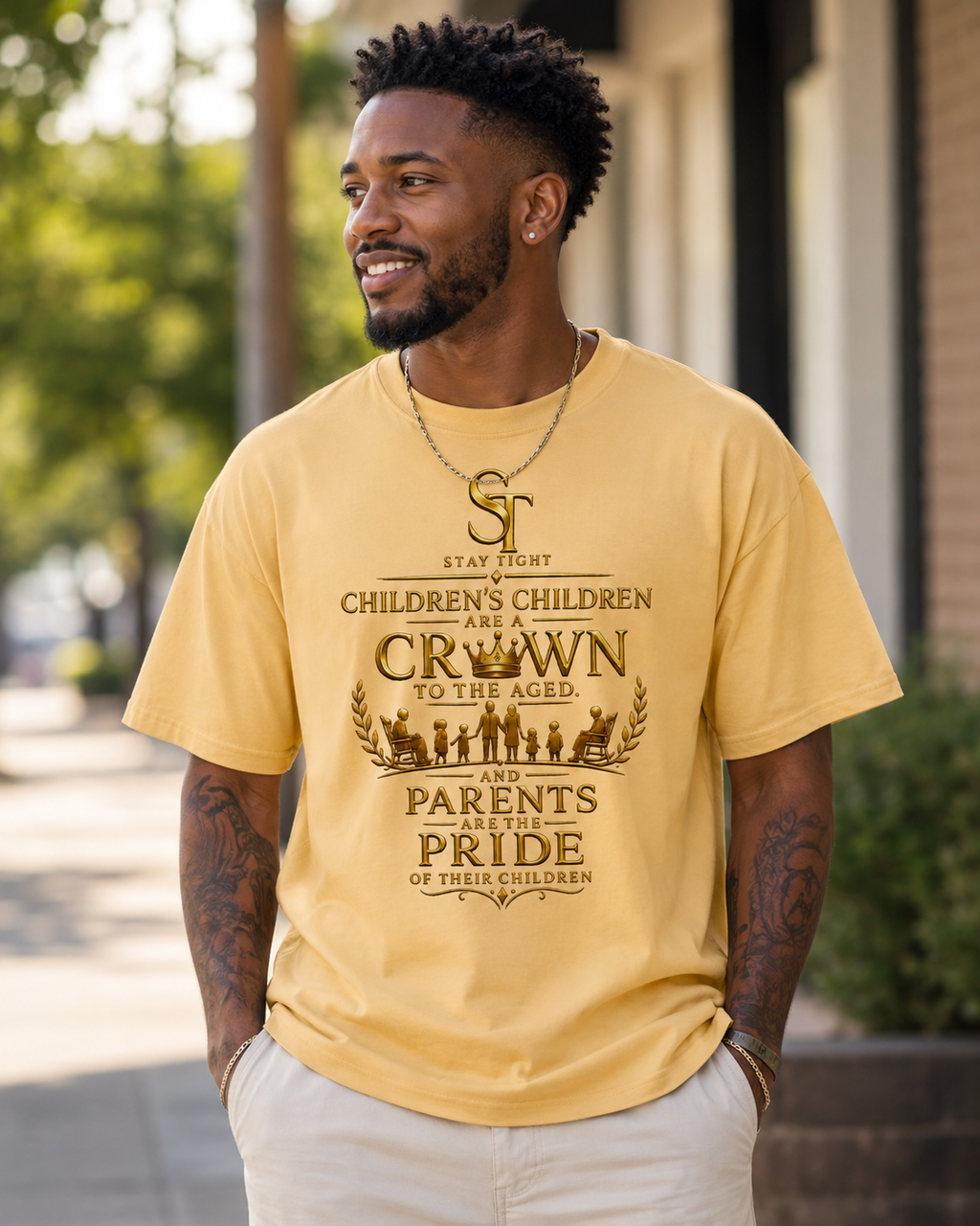 A man wearing a mustard yellow graphic t-shirt with a brown text design that reads 'STAY HUNT CHILDREN'S CHILDREN ARE CROWNED TO THE AGED AND PARENTS ARE PRIDE OF THEIR CHILDREN' with a small illustration of children on the front. He is wearing light beige pants and standing outdoors on a sidewalk.