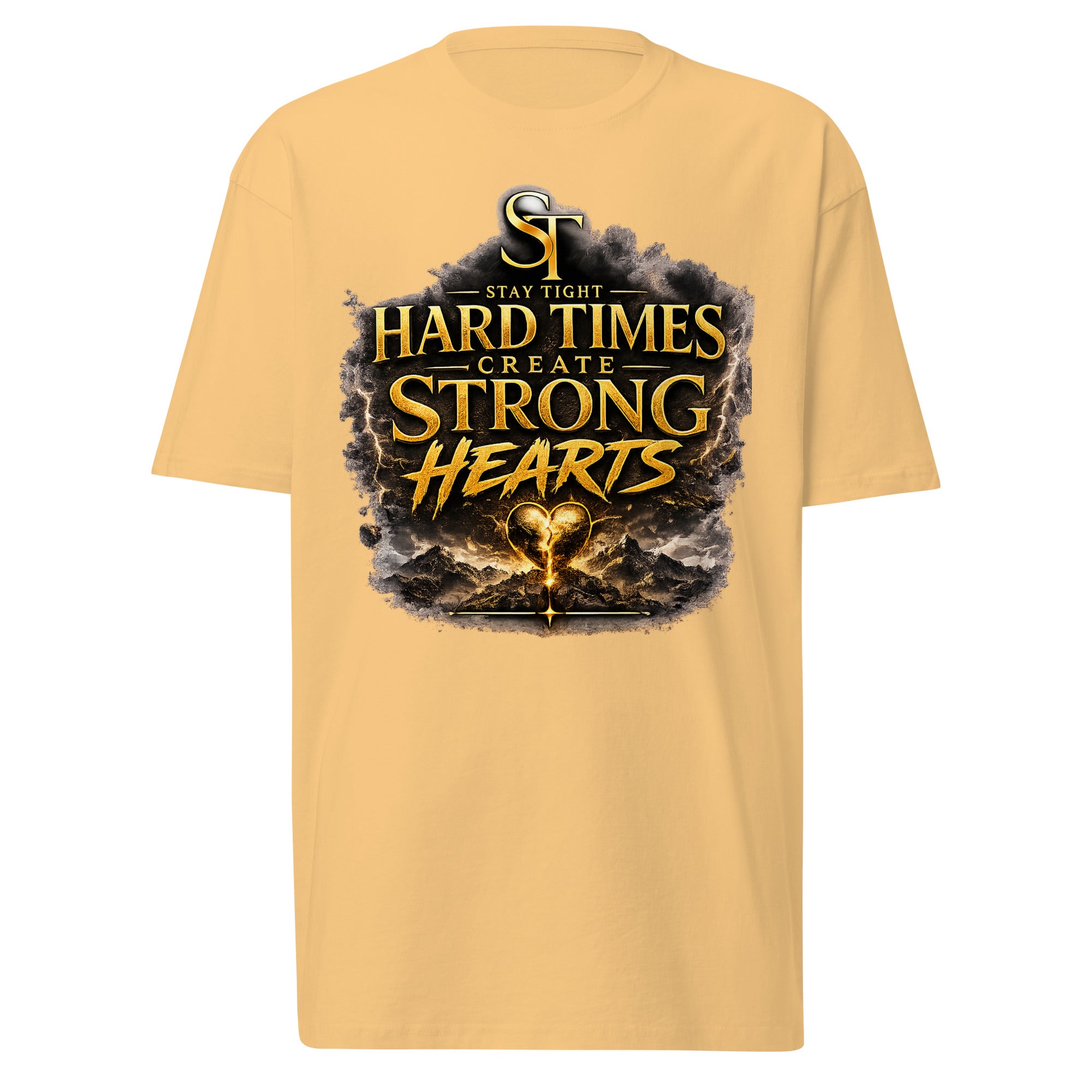Stay Tight premium heavyweight T-shirt featuring the motivational phrase "Hard Times Create Strong Hearts" in bold gold lettering above a glowing heart surrounded by rugged mountains and storm clouds, symbolizing resilience, perseverance, courage, inner strength, and overcoming adversity.